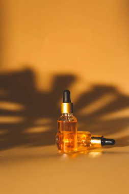 Sarı arka planda kozmetik şişeleriyle gölgeli stüdyo çekimi, cilt bakımı konsepti 