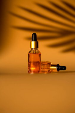 Sarı arka planda kozmetik şişeleriyle gölgeli stüdyo çekimi, cilt bakımı konsepti 