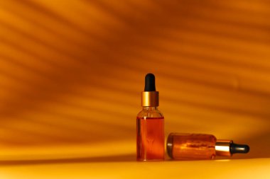 Sarı arka planda kozmetik şişeleriyle gölgeli stüdyo çekimi, cilt bakımı konsepti 