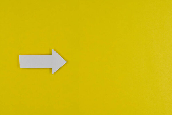 Белая стрелка на желтом бумажном фоне, стрелка в правильном направлении