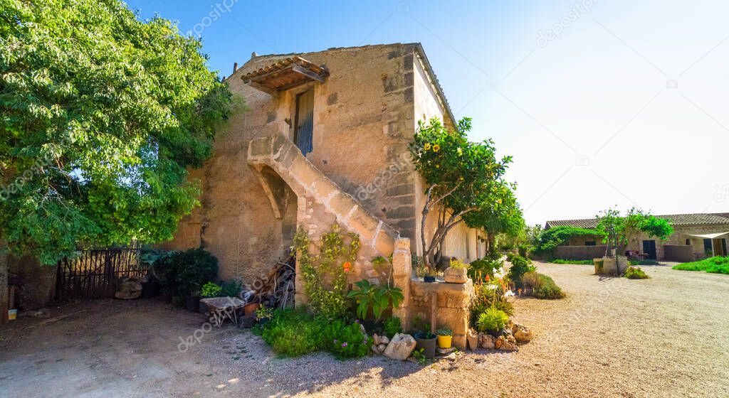 Old spanish farmhouse in inland Mallorca. There are some trees by the house. Bright blue sky