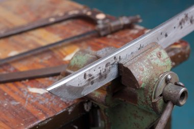 Katana kılıç yontuyor. Bıçak çelik kıskaca sabitlendi..