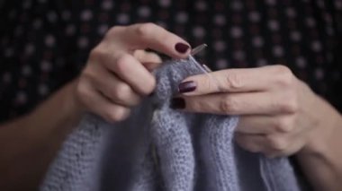 Woman hands knitting handmade wool clothes with knitting needles. Close up view.