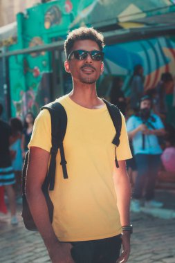 Sarı Gömlekli Yakışıklı Siyah Adam ve Sokak Arkaplanda Gözlüklü Odaklanmamış İnsanlar.