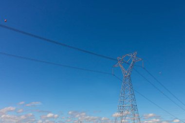 Kırsal kesimdeki yüksek voltajlı bir güç iletim kulesi gün batımında izole edilmiş ve gökyüzünde güzel sıcak bulutlar var. Yaz şehir fotoğrafçılığı. 