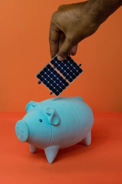 Kumbaraya fotovoltaik güneş paneli yerleştiriliyor. Turuncu arka planda izole edilmiş..