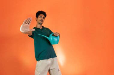 Yeşil gömlekli yakışıklı siyah adam turuncu arka planda bitki tutuyor..