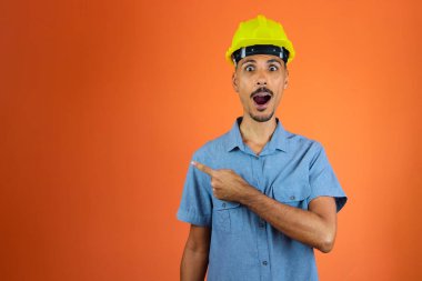 Black Man in Safety Helmet and Blue Shirt isolated on orange.