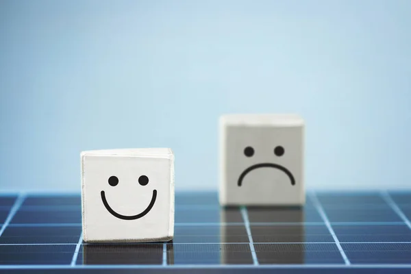 Smile face in bright side and sad face in dark side in wooden block cube on photovoltaic solar panel.