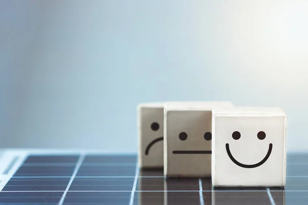 Smile face in bright side and sad face in dark side in wooden block cube on photovoltaic solar panel.