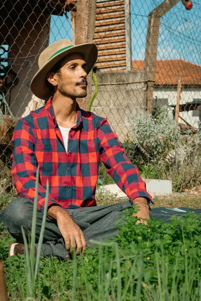 Black farmer beside small modest vegetable garden on sunny day. Farmer With Hat on farm.