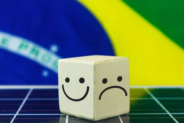 Smile Face and sad face in in wooden block cube and Brazil Flag on photovoltaic solar panel