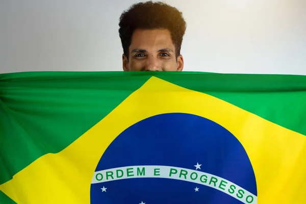 サッカーチームのシャツとブラジルの黒人男性ファンは白に隔離されました カップを祝う旗を持つスポーツファン — ストック写真