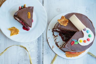 Okul temalı çikolatalı pastanın en üst görünümü şeker palet tokaları ve küçük tabela yaprakları ile süslenmiş.