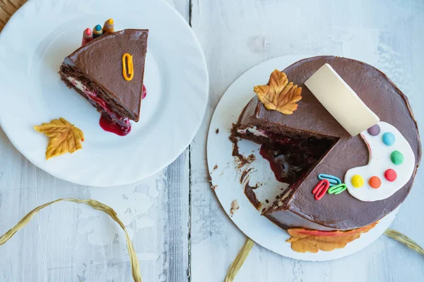 Okul temalı çikolatalı pastanın en üst görünümü şeker palet tokaları ve küçük tabela yaprakları ile süslenmiş.