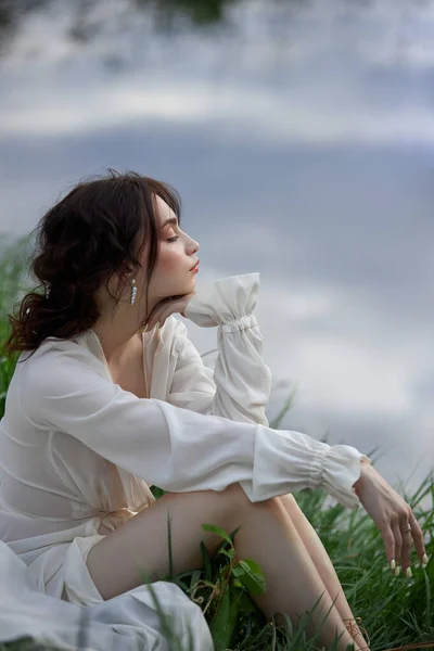 白いドレスの美しい若い女性の海岸湖の池の川に休んでいる カールした髪のプロのメイクやヘアスタイル — ストック写真