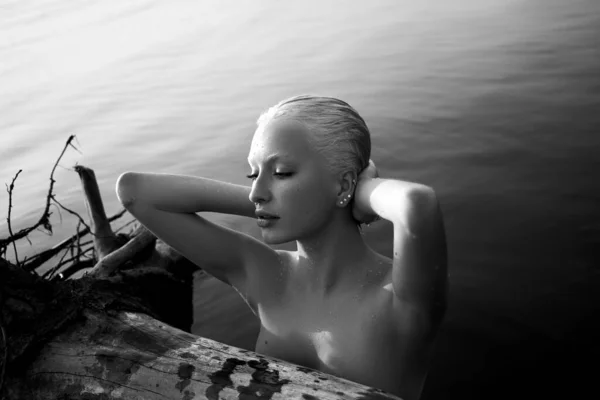 ブロンドの短い髪の女性は海の海岸の水の中に立っている 海岸の水の中でリラックスした女性の芸術的な肖像画 黒と白 — ストック写真