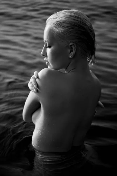 ブロンドの短い髪の女性は海の海岸の水の中に立っている 海岸の水の中でリラックスした女性の芸術的な肖像画 黒と白 — ストック写真