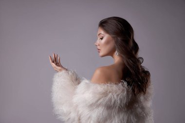 Uzun saçlı, beyaz kürklü, uzun kürklü güzel bir kadının güzel sanat portresi. Bir kadının kulaklarında güzel küpeler. Saç stili, saç stili