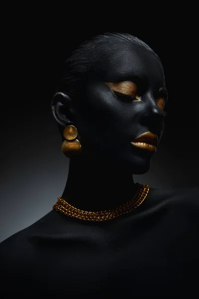 Beauty gold makeup lips eyelids woman black skin color body art, gold jewelry chain, fingertips nails in gold color paint. Professional gold makeup
