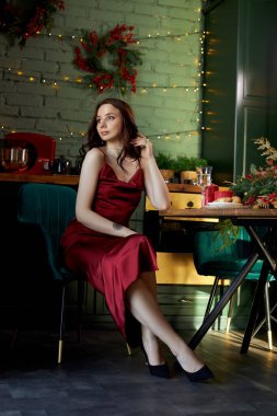 Akşamları mutfakta kırmızı gece lambası elbiseli güzel bir kadın. Duvarda bir çelengin ışıkları parlıyor. Bir kadının arkasında. Güzel, ince bir vücut.