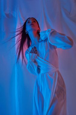 Stüdyoda açık beyaz elbiseli güzel bayan. Neon ışıklı özgürlük konseri. Moda tarzı hafif elbiseler, uzun bacakları olan kadın.