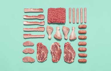 Yeşil naneli bir masada simetrik olarak sıralanmış çeşitli çiğ etle üst manzara. Sosisten bifteğe kadar, barbekü için gerekli malzemelerle donatılmış yiyecek..