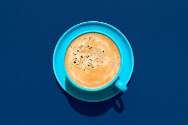 Mavi bir masada bir fincan kahve minimalistiyle manzaranın üstünde. Parlak ışıkta mavi bir fincanda sıcak kahve.