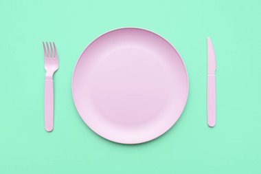Yeşil arka planda boş bir plaka var. Yeşil masadaki pembe çatal bıçak seti, üst manzara..