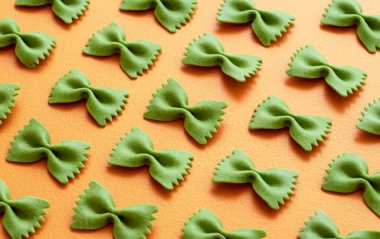 Ispanak farfalle makarnası turuncu bir masaya simetrik olarak dizilmiş. Pişmemiş papyon şekilli makarna ile yakın plan..