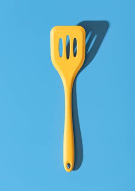 Mavi renkli bir masada sarı silikon bir spatula ile yukarıda. Mavi arka planda parlak ışık minimalisti olan tek bir spatula.