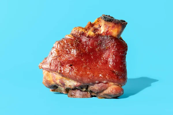 Alman usulü, koyu biralı lezzetli bir domuz budu ile yakın plan. Kızarmış domuz budu, mavi bir arka planda izole edilmiş..