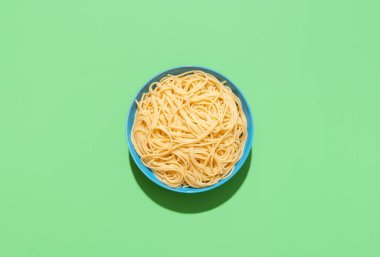 Yukarıda mavi bir tabak ve yeşil bir masada spagetti minimalisti. Sosu olmayan renkli bir arka planda parlak ışıkta spagetti.