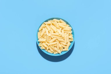 Mavi bir masada makarna kasesi minimalistiyle. Sade pişmiş makarna, sossuz, mavi bir kasede..