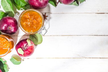 Ev yapımı altın sarısı elma reçeli, çiftlik kırmızı elmaları ve beyaz ahşap arka planda yapraklar kopyalama alanı