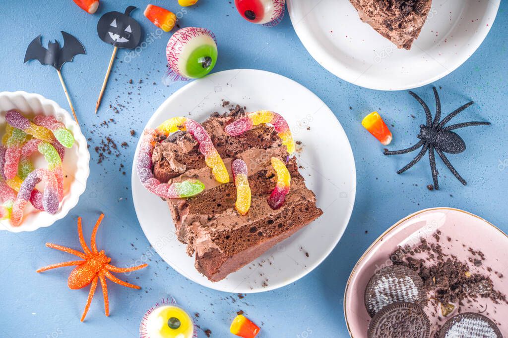 Funny creepy holiday cake for Halloween kids party, Creative dessert idea, chocolate cake piece with marmalade worms, traditional Halloween sweets and candy, copy space