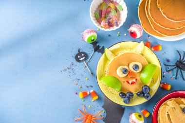 Kahvaltı için yaratıcı ev yapımı Cadılar Bayramı krepleri, komik canavarlar, hayalet, yarasa, cadı şeklinde. Geleneksel şeker ya da şeker, şeker ve süslemelerle, renkli mavi arka planda üst görünüm