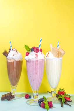 Yaz ferahlatıcı içecekler, milkshake 'ler, dondurmalı çılgın milk shake' ler, böğürtlen, vanilya, çikolata. Parlak mavi bir arka planda 