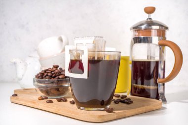 Poşetten taze demlenmiş bir fincan kahve. Süslü kahve çeşitleri, beyaz mutfak masasında fincanlar, kopyalama alanı