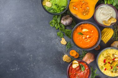 Farklı sonbahar çorbaları seti. Portakal kaselerinde çeşitli sebze çorbaları - mısır, patates, balkabağı, domates, kabak, brokoli kremalı çorba. Siyah beton arkaplanda üst görünüm kopyalama alanı
