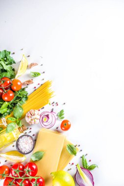 Makarna pişirmek için İtalyan yemekleri. Çeşitli malzemeli çiğ spagetti makarna - soğan, domates, sarımsak, fesleğen, maydanoz, peynir, zeytinyağı. Beyaz tablo arkaplanında, düz kopya alanı