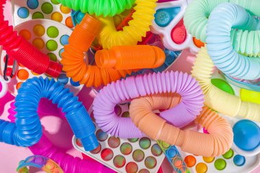 Modern trend çocuklar hareketli parmak oyuncakları, rahatlama konsepti - farklı parlak pop-it setleri, basit gamzeli, yumuşak, pop-tüplü, renkli pembe arka planda, üst görünüm kopyalama alanı