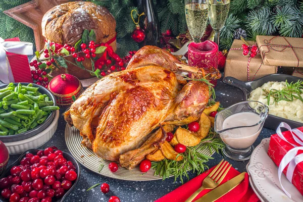 Christmas or New Year turkey dinner. Baked turkey with potato, red berries and sage leaves, on Christmas dinner table with Xmas tree, gift and candles background