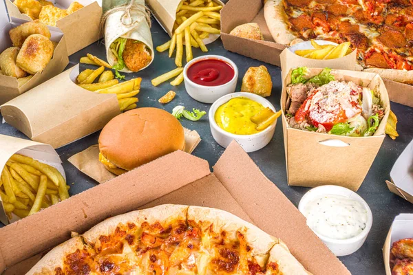 Delivery fastfood ordering food online concept. Large set of assorted take out foods pizza, french fries, fried chicken nuggets, burgers, salads, chicken wings, sides, black concrete background