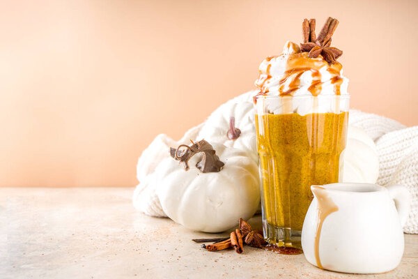 Pumpkin spice latte or milkshake,traditional autumn hot drink with anise, cinnamon, caramel topping, on warm colored background with small decorative pumpkins and cozy sweater, 