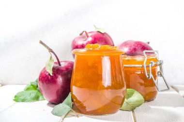 Ev yapımı altın sarısı elma reçeli, çiftlik kırmızı elmaları ve beyaz ahşap arka planda yapraklar kopyalama alanı