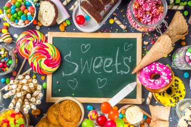 Renkli şekerlerden seç. Çeşitli şekerler, çikolatalar, çörekler, kurabiyeler, lolipoplar, siyah beton arka planda dondurma üst görünümü