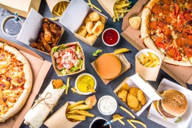 İnternetten fast food siparişi vermek. Muhtelif yemek takımları pizza, patates kızartması, kızarmış tavuk nugget, hamburger, salata, tavuk kanadı, kenarlar, siyah beton arka plan.