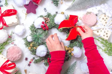 Yumuşak bir Noel konsepti. Dekorasyon malzemeleri, Noel balosu, hediye kutuları, Noel çelengi süsleyen kadınların elleri yapay kar toplarını süslüyor. Noel hazırlama geçmişi
