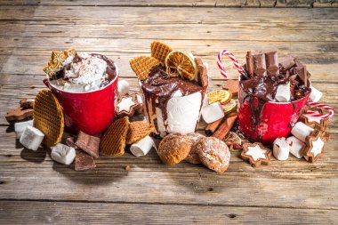 Noel tarzı aşırı yüklü sıcak çikolata bardakları çeşitli malzemelerle çikolata dilimleri, baharatlar, tatlılar, kurabiyeler, şeker ve zencefilli kurabiye, ahşap kaplama kış fotokopi alanı
